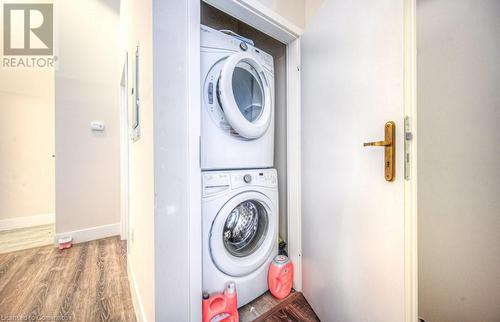 Clothes washing area with hardwood / wood-style floors and stacked washer / dryer - 253 Albert Street N Unit# 104, Waterloo, ON - Indoor Photo Showing Laundry Room