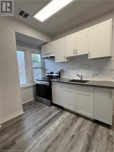 Kitchen with white cabinets, sink, light hardwood / wood-style floors, and stainless steel range oven - 485 Main Street E Unit# 2, Hamilton, ON - Indoor Photo Showing Kitchen