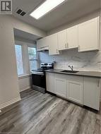 Kitchen with white cabinets, sink, light hardwood / wood-style floors, and stainless steel range oven - 