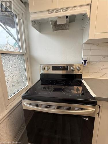 Kitchen with ventilation hood, stainless steel electric range, white cabinetry, and tasteful backsplash - 485 Main Street E Unit# 2, Hamilton, ON - Indoor Photo Showing Kitchen