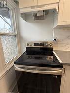 Kitchen with ventilation hood, stainless steel electric range, white cabinetry, and tasteful backsplash - 