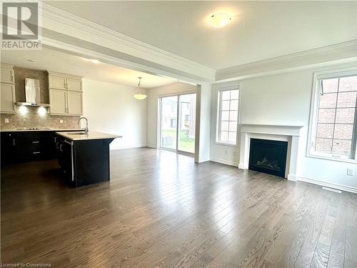 Kitchen featuring dark hardwood / wood-style flooring, tasteful backsplash, ornamental molding, a kitchen island with sink, and wall chimney range hood - 94 Milt Schmidt Street, Kitchener, ON - Indoor With Fireplace