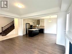 Kitchen featuring hardwood / wood-style floors, a kitchen island with sink, crown molding, stainless steel fridge, and decorative light fixtures - 