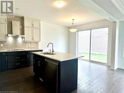 Kitchen featuring stainless steel dishwasher, wall chimney exhaust hood, sink, white cabinetry, and an island with sink - 