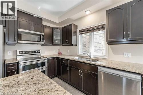 Kitchen featuring appliances with stainless steel finishes, light stone counters, dark brown cabinets, sink, and light tile patterned floors - 243 Greenwater Place Unit# Upper, Kitchener, ON - Indoor Photo Showing Kitchen With Double Sink