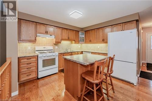 Kitchen with white appliances, backsplash, a kitchen breakfast bar, light wood-type flooring, and a kitchen island - 435 Shadow Wood Crescent, Waterloo, ON - Indoor Photo Showing Kitchen