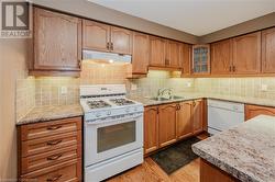 Kitchen with light wood-type flooring, backsplash, light stone counters, white appliances, and sink - 