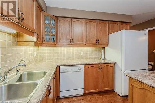 Kitchen featuring light stone countertops, decorative backsplash, white appliances, sink, and light hardwood / wood-style floors - 435 Shadow Wood Crescent, Waterloo, ON - Indoor Photo Showing Kitchen With Double Sink