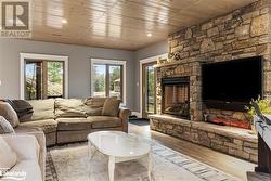 Living room with a stone fireplace, wooden ceiling, and light wood-type flooring - 