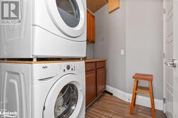 Clothes washing area with dark hardwood / wood-style flooring, stacked washer and dryer, and cabinets - 