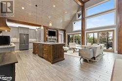 Kitchen with stainless steel appliances, high vaulted ceiling, beamed ceiling, hanging light fixtures, and an island with sink - 