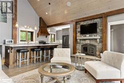 Living room featuring a stone fireplace, high vaulted ceiling, wooden ceiling, and light wood-type flooring - 