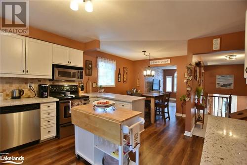 Kitchen with white cabinets, dark hardwood / wood-style floors, decorative light fixtures, light stone counters, and stainless steel appliances - 97 Glen Eton Road, Wasaga Beach, ON 