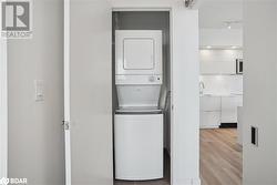 Laundry area with sink, stacked washer and clothes dryer, and light wood-type flooring - 