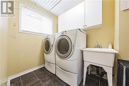 Clothes washing area with cabinets, dark tile patterned floors, and washing machine and dryer - 145 Dragoon Drive, Hamilton, ON - Indoor Photo Showing Laundry Room