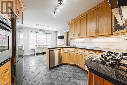 Kitchen with sink, kitchen peninsula, dark stone counters, decorative backsplash, and appliances with stainless steel finishes - 145 Dragoon Drive, Hamilton, ON - Indoor Photo Showing Kitchen