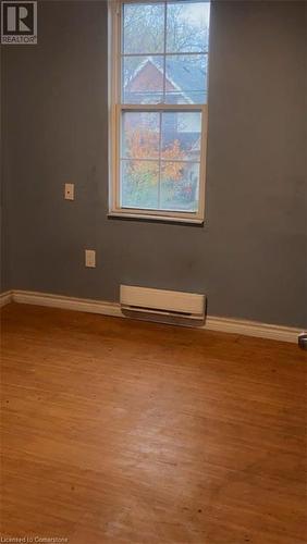 Empty room with wood-type flooring, plenty of natural light, and a baseboard heating unit - 49 Robins Avenue Unit# 3, Hamilton, ON 