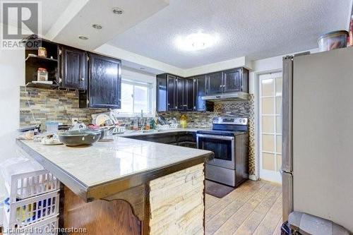 Kitchen with stainless steel appliances, light hardwood / wood-style flooring, kitchen peninsula, a kitchen bar, and decorative backsplash - 539 Briarwood Avenue, Listowel, ON - Indoor Photo Showing Kitchen