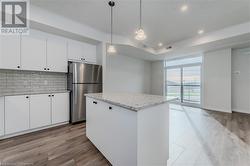 Kitchen with white cabinets, decorative light fixtures, stainless steel refrigerator, and light hardwood / wood-style flooring - 