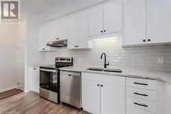 Kitchen featuring white cabinetry, sink, light stone counters, appliances with stainless steel finishes, and light wood-type flooring - 