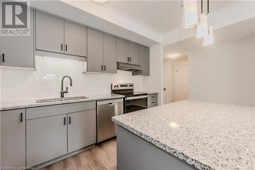 Kitchen with sink, light stone counters, light hardwood / wood-style floors, pendant lighting, and appliances with stainless steel finishes - 142 Foamflower Place Unit# D053, Waterloo, ON - Indoor Photo Showing Kitchen With Double Sink With Upgraded Kitchen