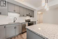 Kitchen with sink, light stone counters, light hardwood / wood-style floors, pendant lighting, and appliances with stainless steel finishes - 