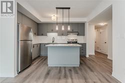 Kitchen featuring hanging light fixtures, stainless steel appliances, light hardwood / wood-style flooring, gray cabinets, and a kitchen island - 