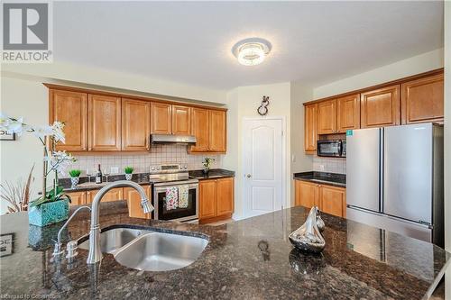 Kitchen featuring dark stone countertops, sink, appliances with stainless steel finishes, and tasteful backsplash - 584 Winterburg Walk, Waterloo, ON - Indoor Photo Showing Kitchen With Double Sink