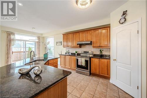 Kitchen featuring sink, tasteful backsplash, dark stone countertops, stainless steel electric stove, and light tile patterned floors - 584 Winterburg Walk, Waterloo, ON - Indoor Photo Showing Kitchen With Double Sink