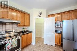 Kitchen with decorative backsplash, light tile patterned flooring, dark stone counters, and appliances with stainless steel finishes - 