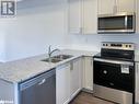 Kitchen featuring white cabinetry, sink, dark wood-type flooring, stainless steel appliances, and light stone counters - 1581 Rose Way Unit# 513, Milton, ON  - Indoor Photo Showing Kitchen With Stainless Steel Kitchen With Double Sink With Upgraded Kitchen 