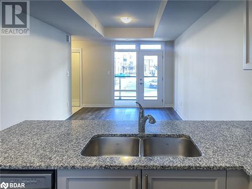 Kitchen featuring dishwasher, sink, dark hardwood / wood-style floors, a tray ceiling, and stone countertops - 1581 Rose Way Unit# 513, Milton, ON - Indoor Photo Showing Kitchen With Double Sink