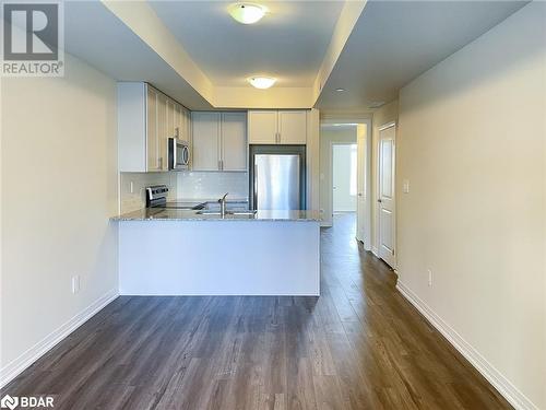 Kitchen with light stone countertops, appliances with stainless steel finishes, tasteful backsplash, dark hardwood / wood-style flooring, and kitchen peninsula - 1581 Rose Way Unit# 513, Milton, ON - Indoor Photo Showing Kitchen