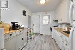 Kitchen with a textured ceiling, white cabinets, light hardwood / wood-style floors, and white appliances - 