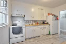 Kitchen featuring light hardwood / wood-style floors, white cabinetry, white appliances, and exhaust hood - 