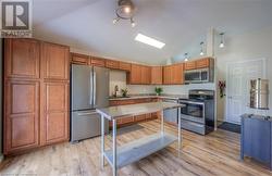 Kitchen with appliances with stainless steel finishes, light wood-type flooring, vaulted ceiling, and sink - 