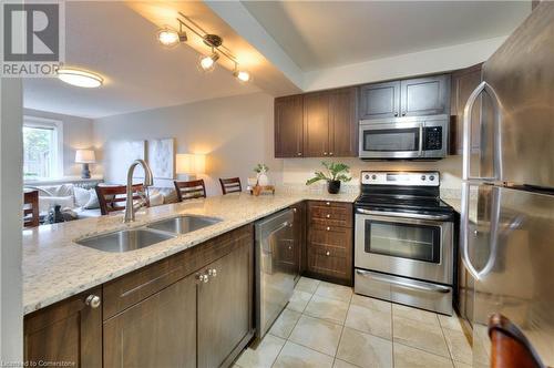 Kitchen featuring sink, stainless steel appliances, light stone counters, dark brown cabinets, and light tile patterned floors - 276 Eiwo Court Unit# 105, Waterloo, ON - Indoor Photo Showing Kitchen With Stainless Steel Kitchen With Double Sink