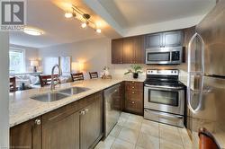 Kitchen featuring sink, stainless steel appliances, light stone counters, dark brown cabinets, and light tile patterned floors - 