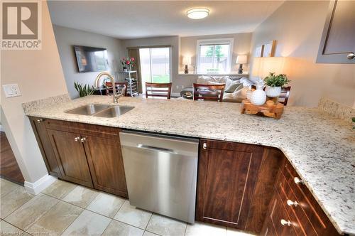 Kitchen featuring sink, light stone counters, stainless steel dishwasher, dark brown cabinets, and light tile patterned floors - 276 Eiwo Court Unit# 105, Waterloo, ON - Indoor Photo Showing Kitchen With Double Sink