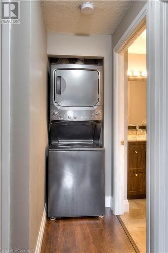 Washroom featuring hardwood / wood-style flooring, sink, stacked washer / dryer, and a textured ceiling - 276 Eiwo Court Unit# 105, Waterloo, ON - Indoor Photo Showing Laundry Room