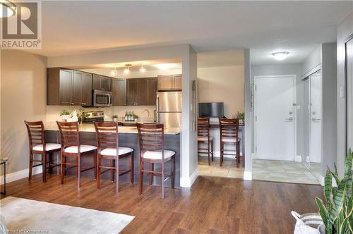 Kitchen featuring dark brown cabinetry, light hardwood / wood-style flooring, kitchen peninsula, a kitchen bar, and appliances with stainless steel finishes - 276 Eiwo Court Unit# 105, Waterloo, ON - Indoor Photo Showing Kitchen