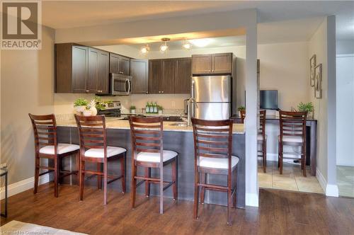 Kitchen with dark brown cabinetry, stainless steel appliances, light stone counters, a breakfast bar, and hardwood / wood-style flooring - 276 Eiwo Court Unit# 105, Waterloo, ON - Indoor Photo Showing Kitchen