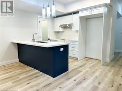 Kitchen with light wood-type flooring, ventilation hood, sink, decorative light fixtures, and white cabinets - 