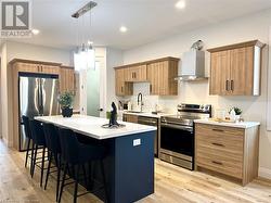 Kitchen with wall chimney exhaust hood, a kitchen island, appliances with stainless steel finishes, and light hardwood / wood-style flooring - 