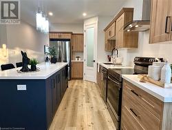 Kitchen with sink, wall chimney exhaust hood, appliances with stainless steel finishes, decorative light fixtures, and a kitchen island - 