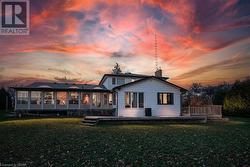 Back house at dusk with a sunroom, a deck, and a lawn - 