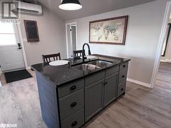 Kitchen with a wall mounted AC, a kitchen island with sink, sink, and light wood-type flooring - 