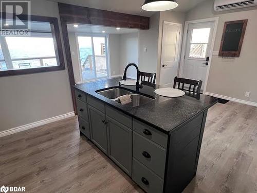 Kitchen featuring sink, an AC wall unit, dark stone countertops, a kitchen island with sink, and light wood-type flooring - 80 Ridley Street, Prince Edward County, ON - Indoor Photo Showing Kitchen With Double Sink