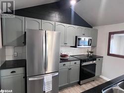 Kitchen with backsplash, light hardwood / wood-style floors, lofted ceiling, white cabinets, and appliances with stainless steel finishes - 