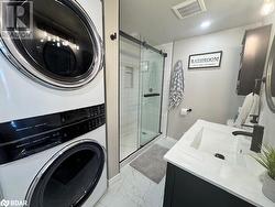 Bathroom featuring vanity, stacked washer and clothes dryer, and walk in shower - 